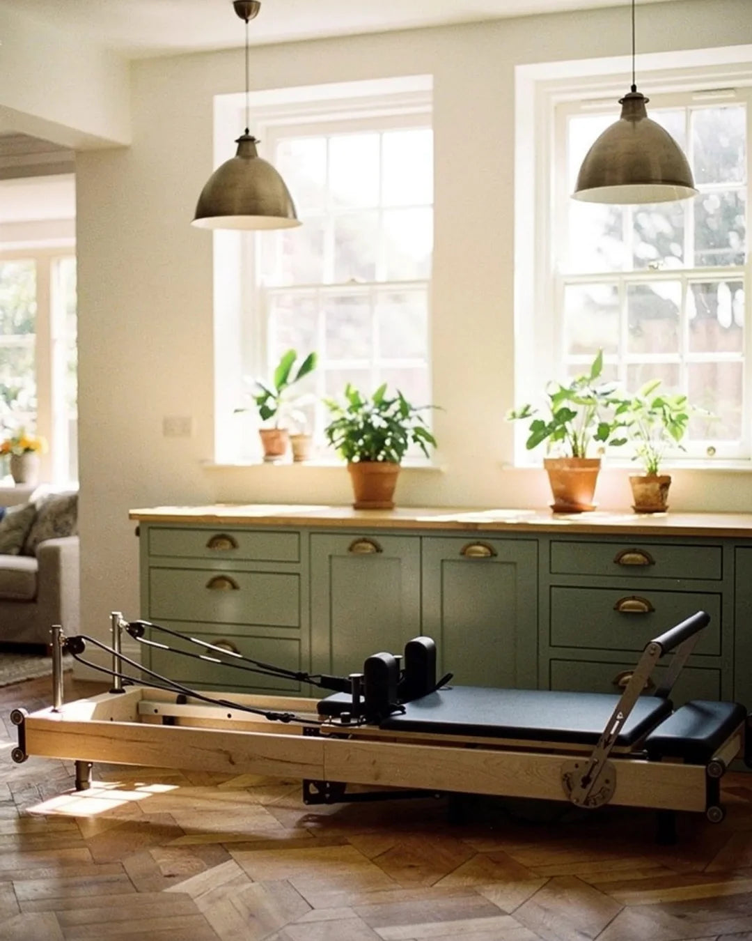Pilates reformer machine in a room with large windows and green cabinets.