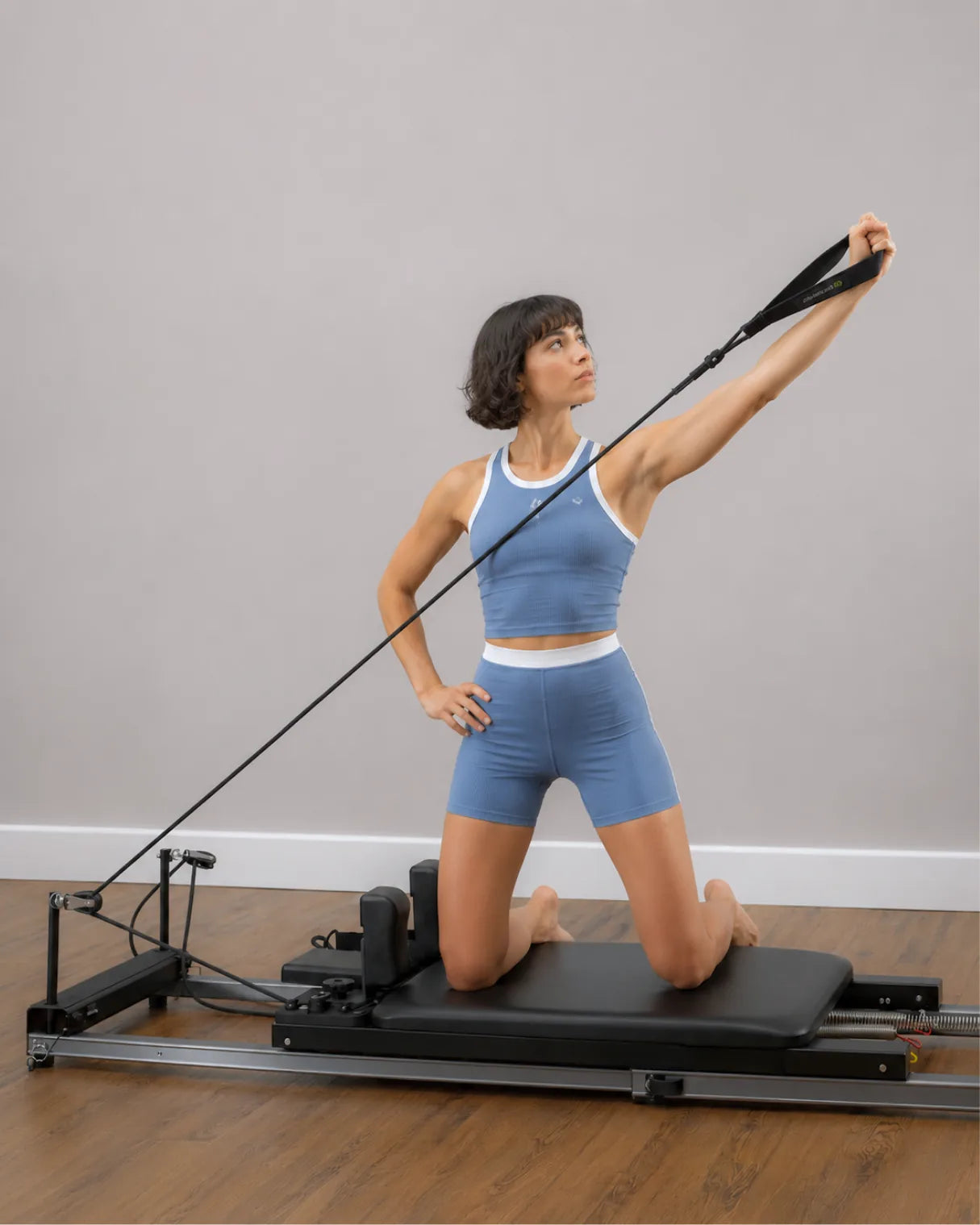 Mujer realizando remo de rodillas en un Reformer de Pilates para casa